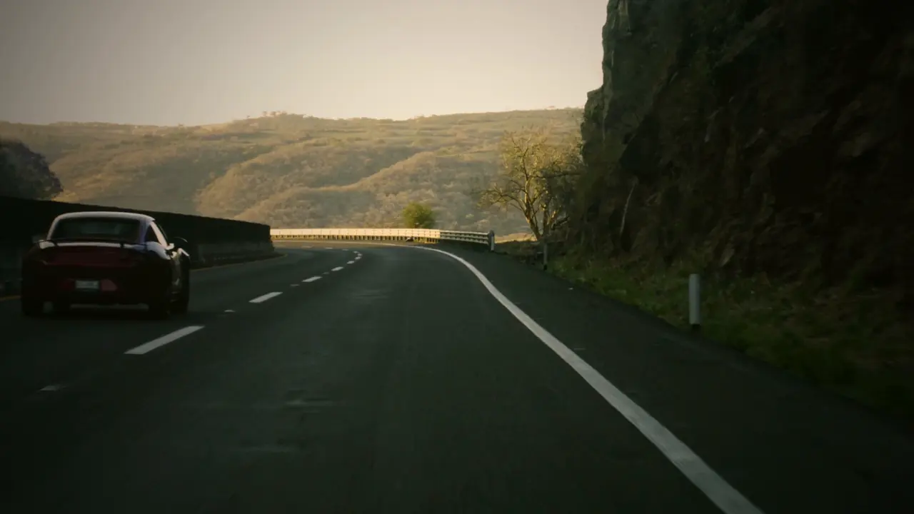 A sports car on a curving highway through the hills at dusk